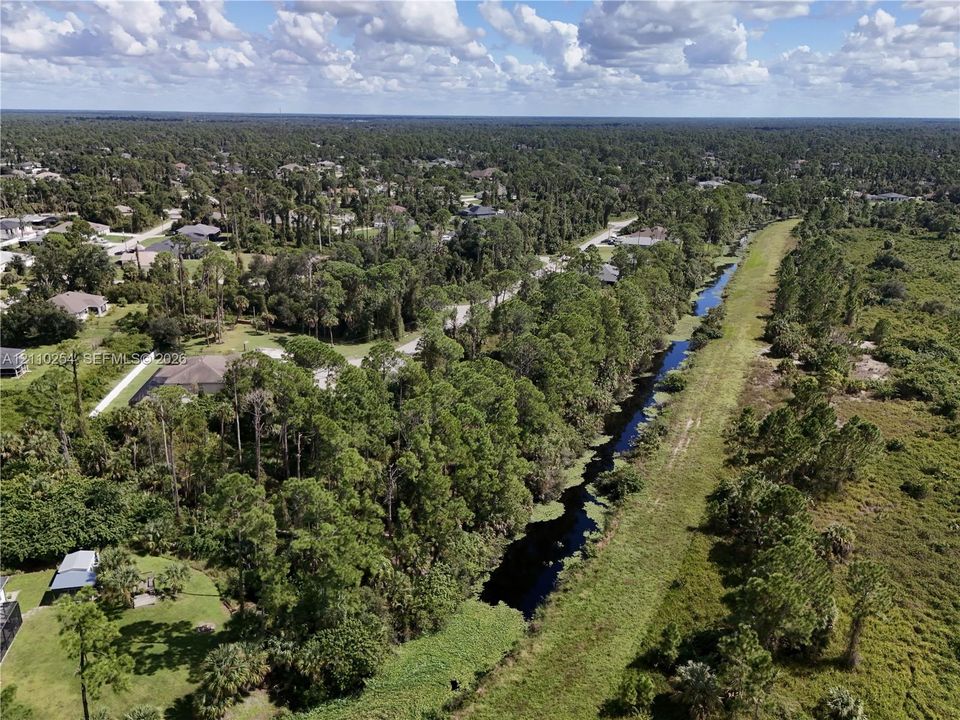 Aerial perspective of a parcel featuring mature trees, native vegetation, and a canal
