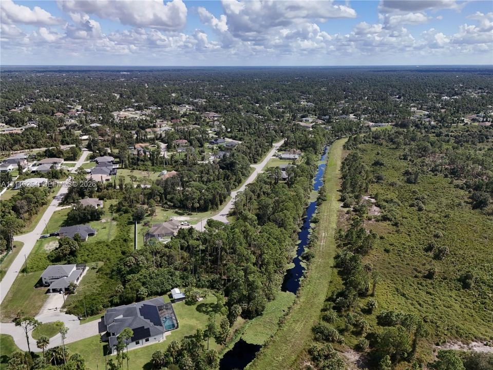 Aerial perspective featuring a residential setting with expansive natural surroundings, mature tree lines, and a bordering waterway