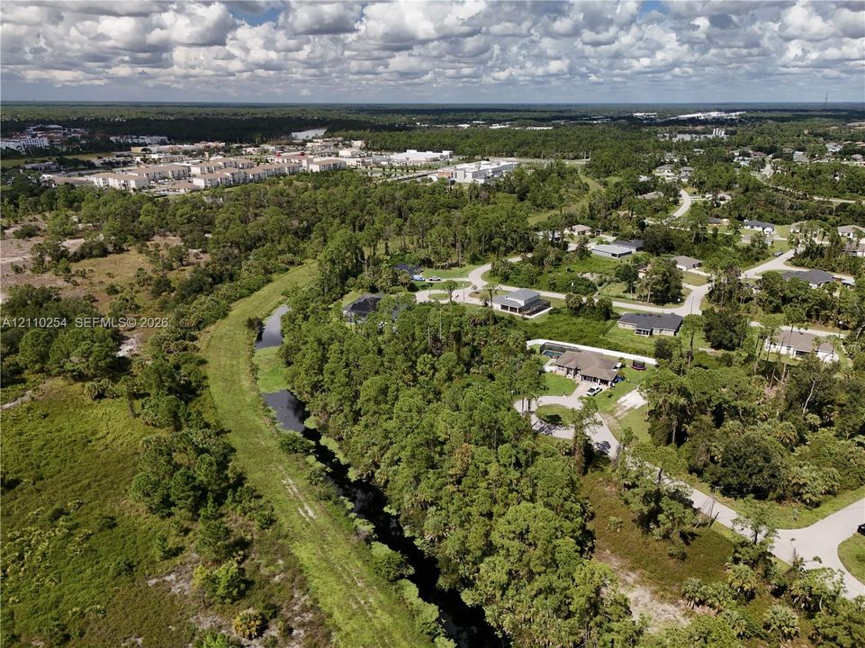 Aerial perspective featuring surrounding woodland, natural waterway, paved thoroughfares, and proximity to regional infrastructure