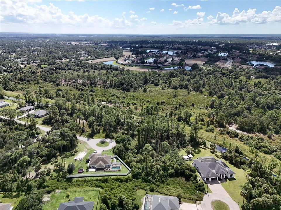 Aerial perspective showcasing a residential property with a private swimming pool, fenced perimeter, multi-car garage, and established tree-lined landscaping within a suburban setting