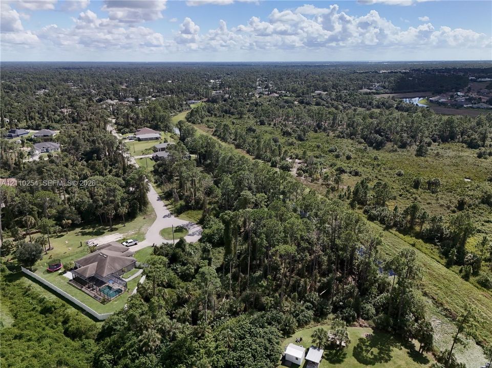 Aerial perspective of a property featuring a private swimming pool, fenced backyard, and surrounding mature wooded landscape