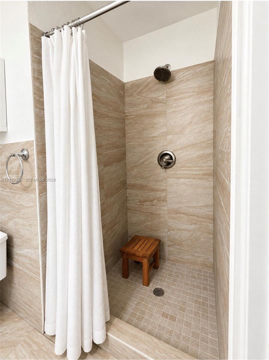 Walk-in shower featuring floor-to-ceiling neutral stone-finish tile surround, a mosaic tile floor, and a circular brushed-metal shower fixture