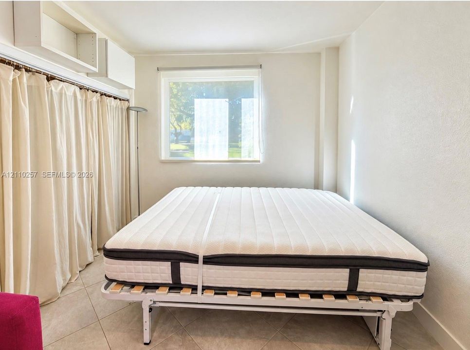 Neutral-toned room featuring large-format ceramic tile flooring, built-in white overhead cabinetry, and a rectangular window