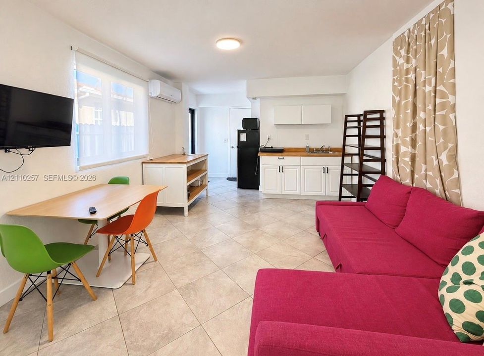 Open-concept kitchen area featuring white shaker-style cabinetry, wood-finish countertops, tiled flooring, and a wall-mounted climate control unit