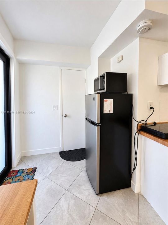 Kitchen area featuring diagonal-set ceramic tile flooring, stainless steel and black refrigerator, black countertop microwave, and wood-surface counter