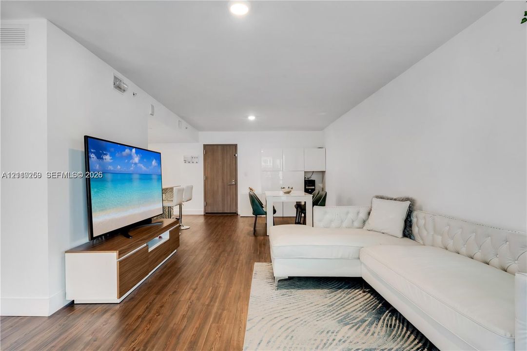 Open-concept living space featuring wood-finish flooring, recessed lighting, and high-gloss white built-in cabinetry
