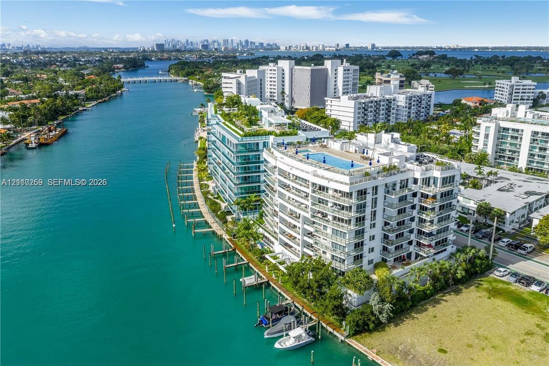 Waterfront multi-story residential building featuring a rooftop pool, private deep-water boat slips, expansive glass-railed balconies, and extensive perimeter landscaping
