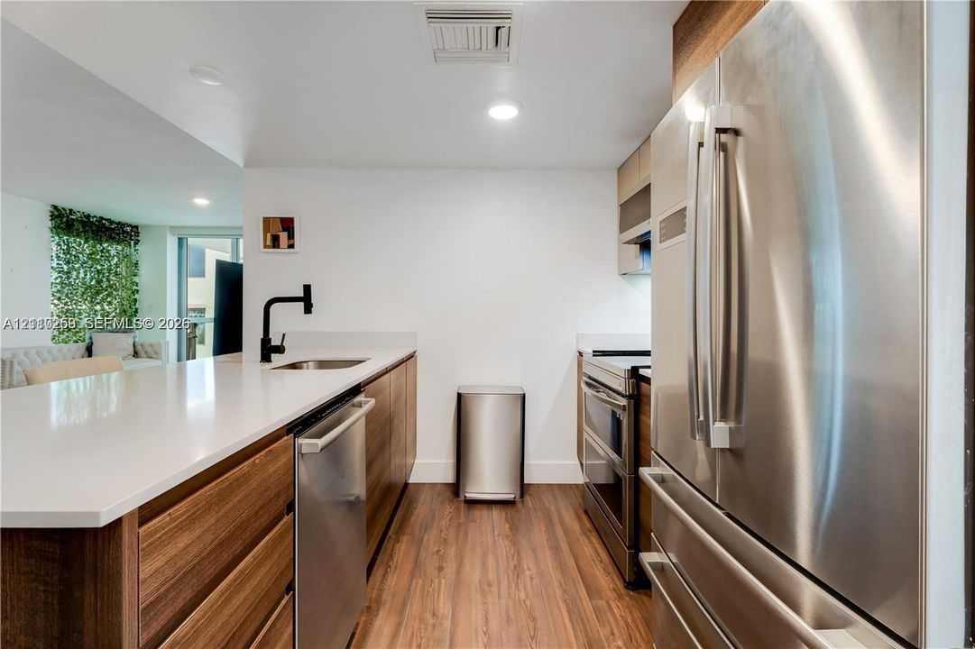 Kitchen featuring stainless steel appliances, wood-finish cabinetry, white solid-surface countertops, wood-finish flooring, and a matte black faucet
