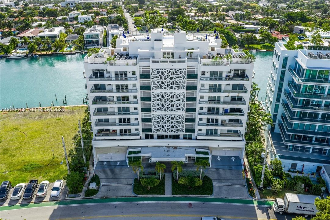 Waterfront high-rise building featuring decorative facade screening, private balcony levels, ground-level covered parking, and palm tree landscaping