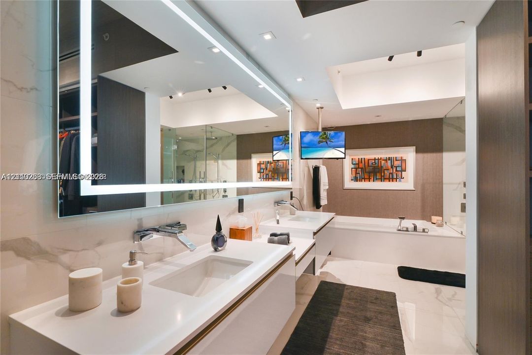 Dual floating vanities with integrated sinks, large LED-backlit mirror, recessed ceiling lighting, deep soaking tub, and walk-in glass shower