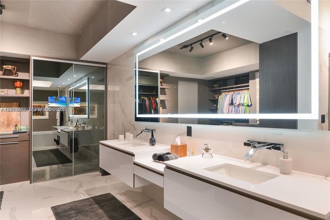 Double floating vanity with integrated rectangular sinks, expansive LED-backlit mirror, wall-mounted chrome faucets, and large-format porcelain tile flooring