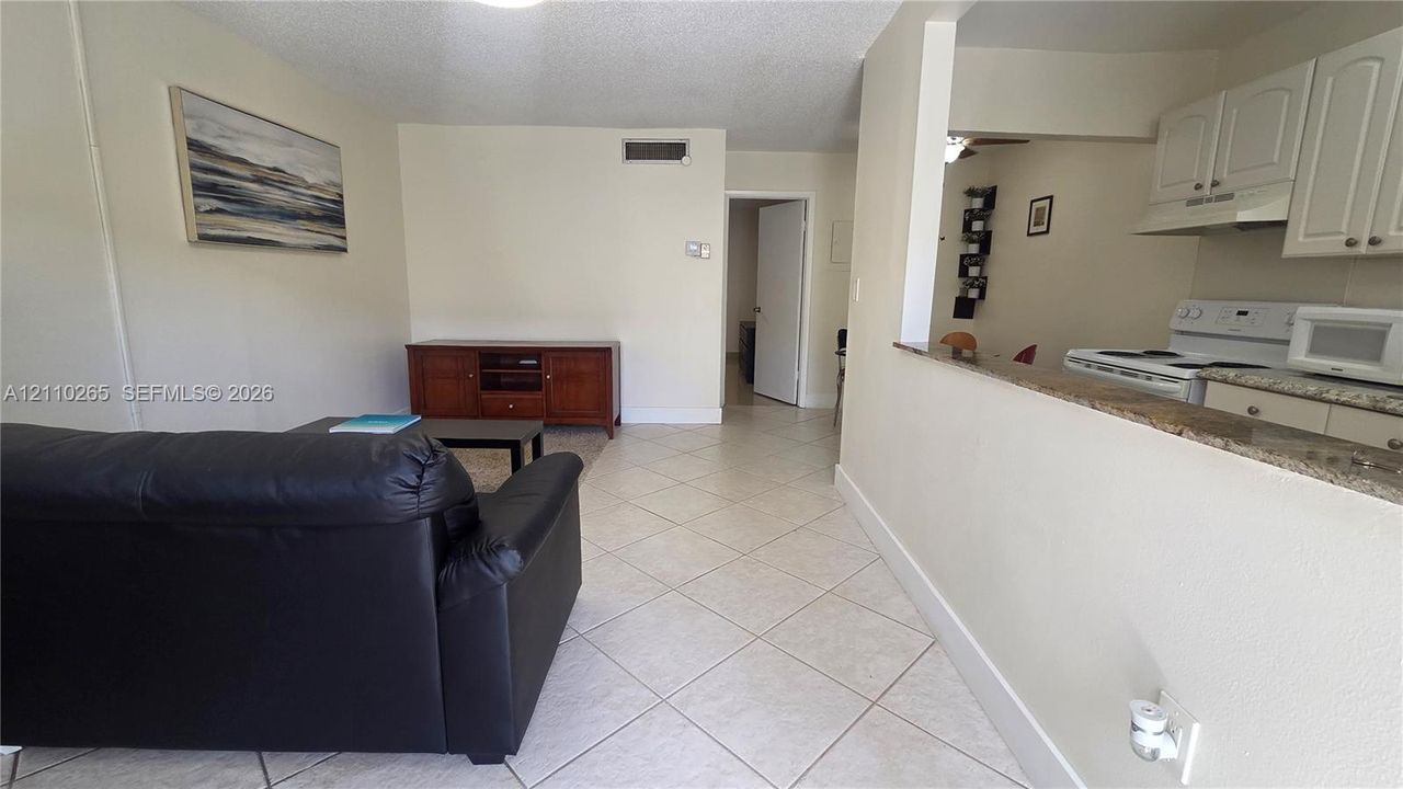Interior featuring diagonal ceramic tile flooring, kitchen pass-through window with a stone-finish countertop, and white shaker-style cabinetry