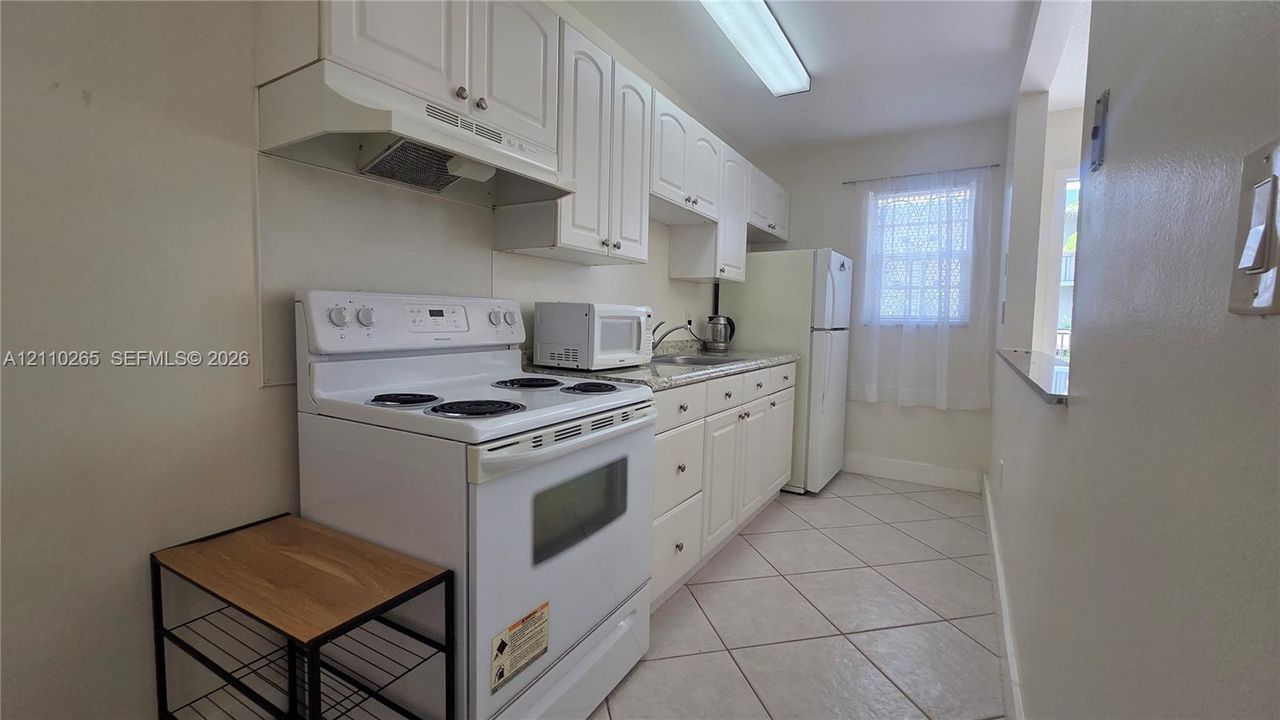 Kitchen featuring white cabinetry, stone-surface countertops, tile flooring, and integrated white appliances