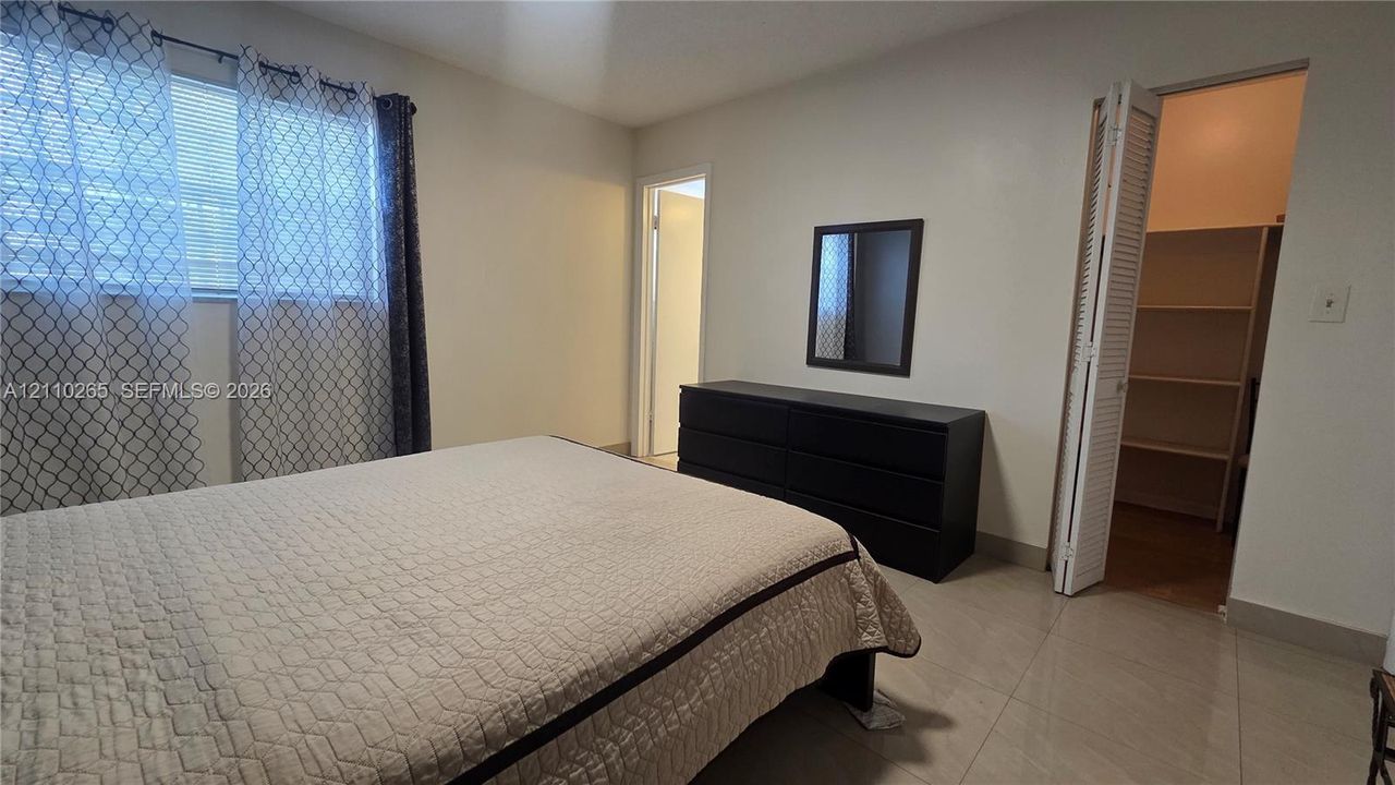 Neutral wall tones, horizontal window blinds, large-format tile flooring, and walk-in closet featuring built-in shelving