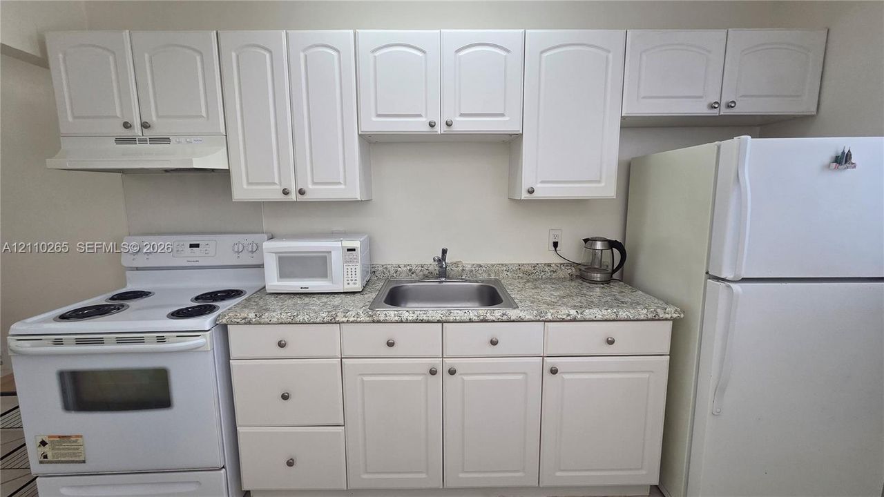 Kitchen area featuring white shaker-style cabinetry, stone-finish countertops, stainless steel sink with a chrome faucet, and white electric range