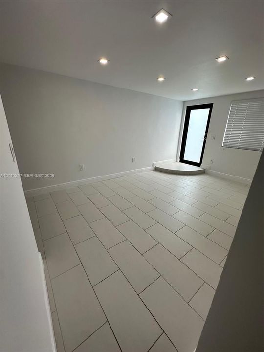 Neutral interior space featuring large-format ceramic tile flooring, recessed ceiling lighting, and a glass-paneled door with a semi-circular threshold step