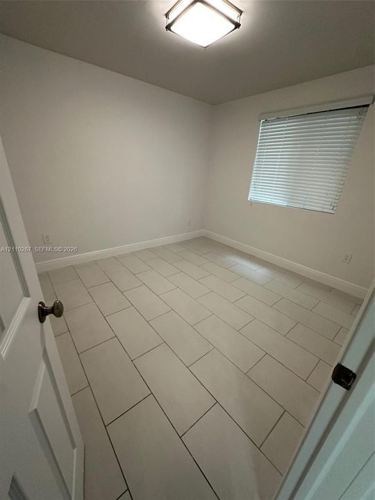 Neutral-toned tile flooring, square-patterned flush-mount ceiling lighting, and horizontal window blinds