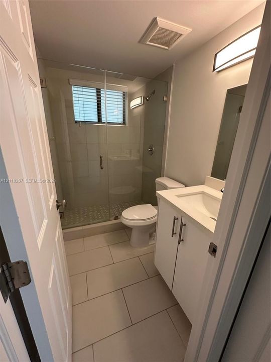 Bathroom featuring a white vanity cabinet with a stone-surface countertop, walk-in shower with a frameless glass enclosure, tiled flooring, and modern wall-mounted lighting