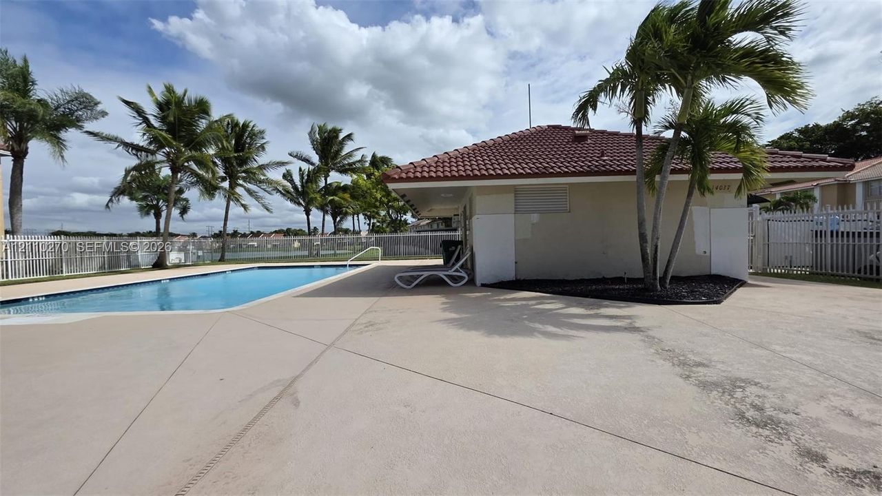 In-ground swimming pool with concrete decking, tile roof, and perimeter fencing