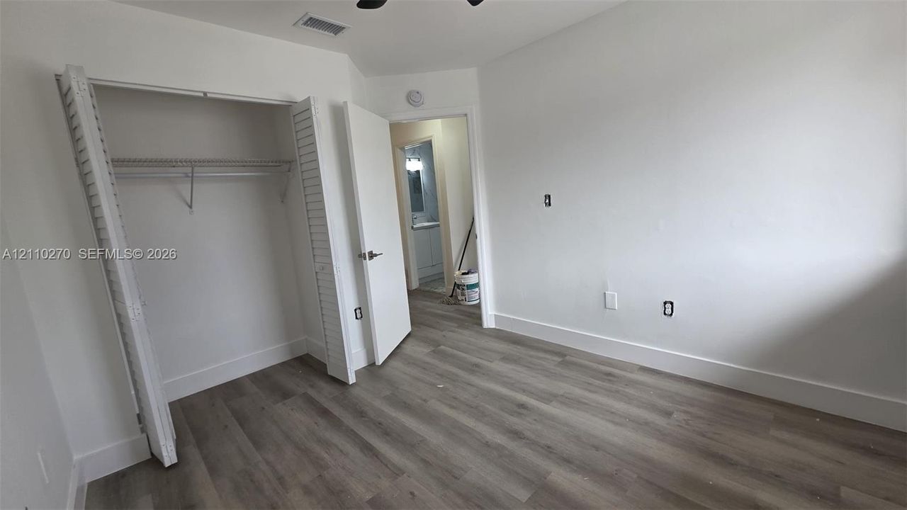 Neutral-toned interior space featuring wood-finish flooring, white walls, and a built-in closet with louvered doors