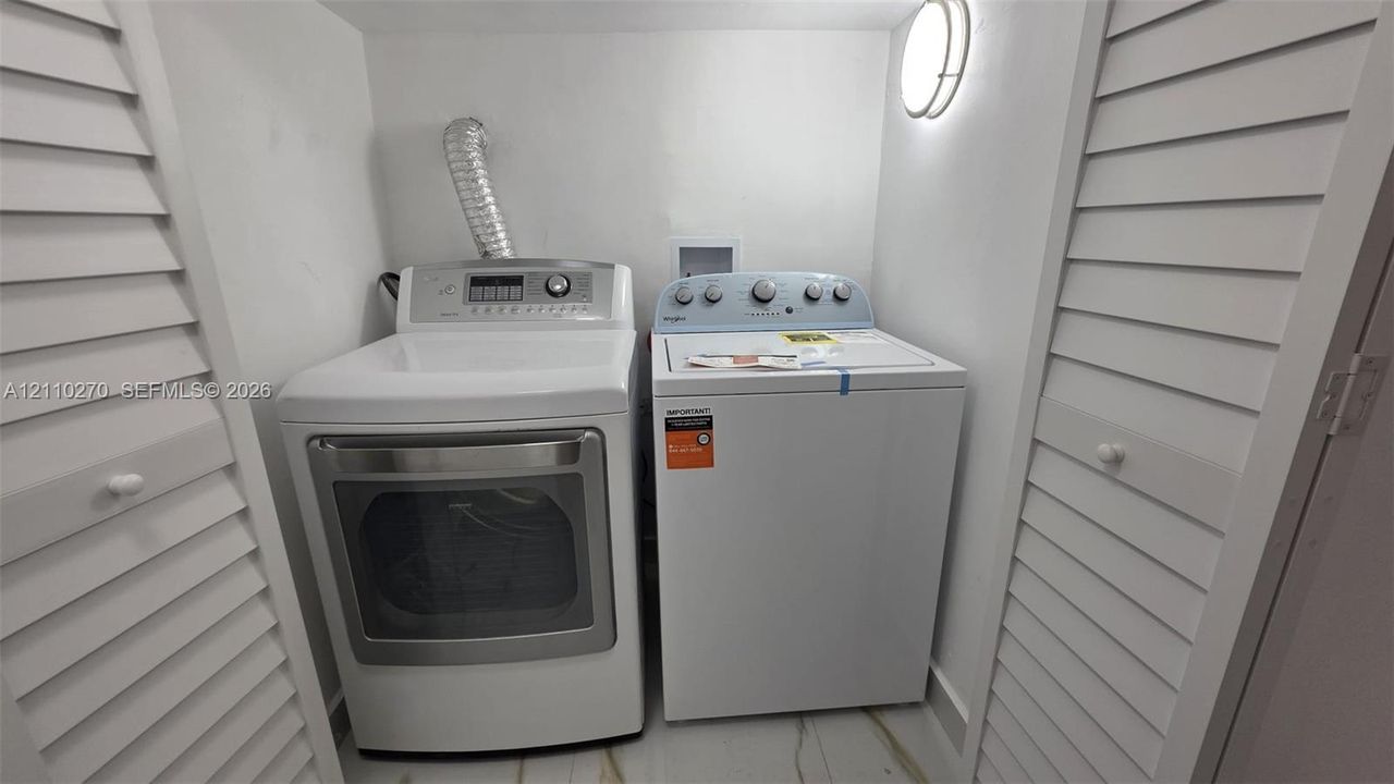 Laundry space featuring dual white louvered closet doors, a top-loading washing machine, a front-loading dryer, and a wall-mounted circular light fixture