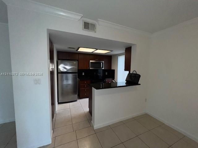Kitchen featuring dark wood cabinetry, stainless steel appliances, black countertops, and tile flooring