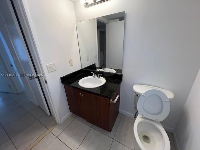 Vanity featuring a dark stone countertop, integrated sink, wood-finish cabinetry, a full-height wall mirror, and tile flooring