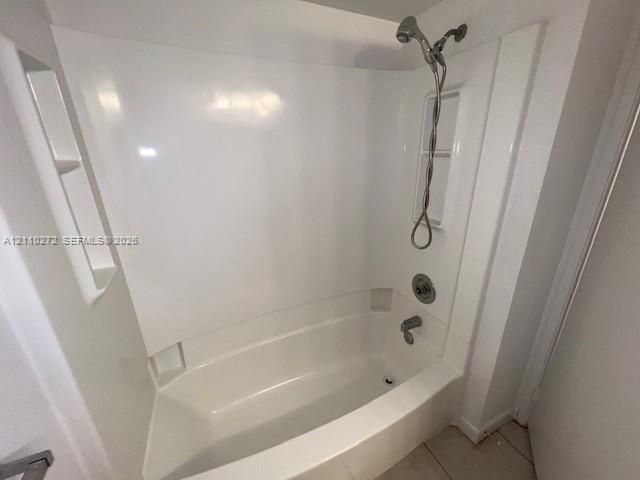 Bathtub and shower combination featuring a glossy white surround, integrated shelving niches, and a polished metallic handheld shower fixture