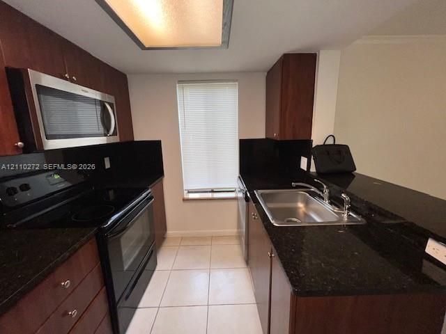 Kitchen featuring dark wood cabinetry, black countertops, a stainless steel undermount sink, and integrated black appliances