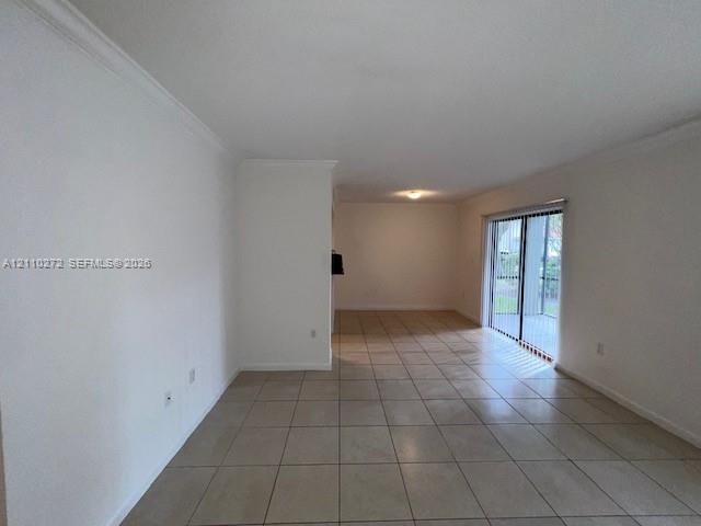 Open-concept interior featuring neutral ceramic tile flooring, crown molding, and a sliding glass door providing external access