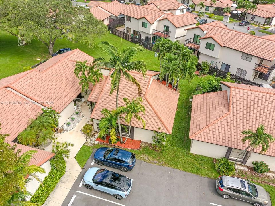 Aerial view featuring terracotta-style roof tiles, mature palm trees, designated parking spaces, and landscaped exterior grounds