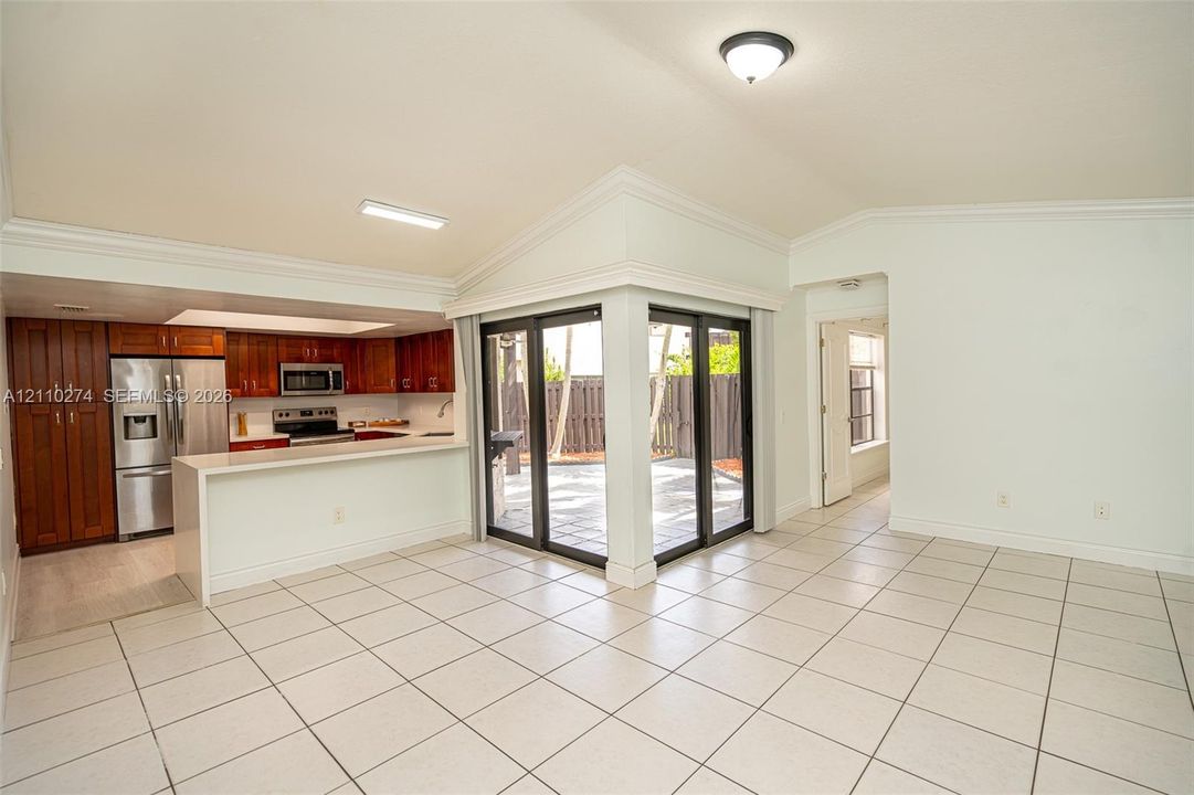 Kitchen featuring wood cabinetry, stainless steel appliances, and a breakfast bar, with vaulted ceilings and sliding glass doors opening to a paved exterior space