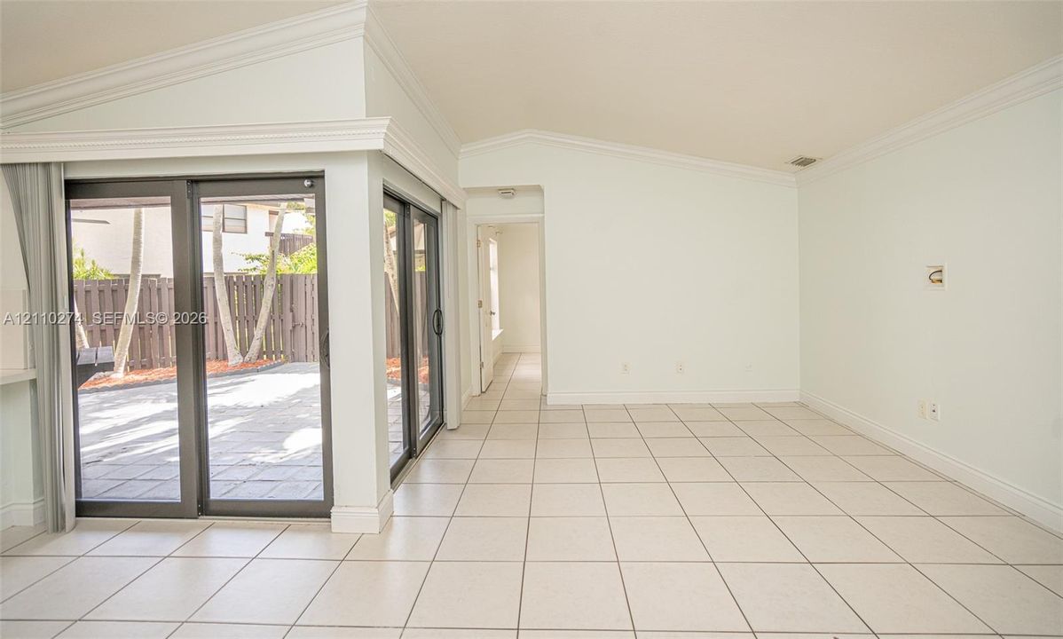 Vaulted ceiling featuring crown molding, ceramic tile flooring, and sliding glass doors with dark frames