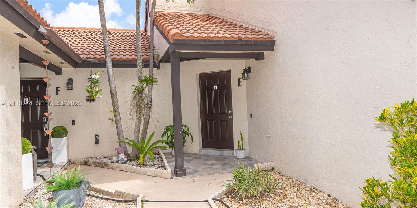 Exterior entryway featuring a stucco facade, clay tile roof, dark-finished entry doors, and a stone-paver walkway