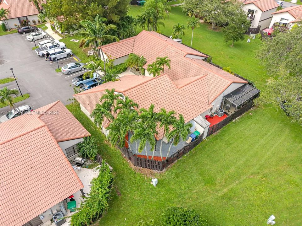 Aerial perspective of a residence featuring a clay tile roof, a screened-in patio, and fenced-in hardscaped areas surrounded by manicured grounds