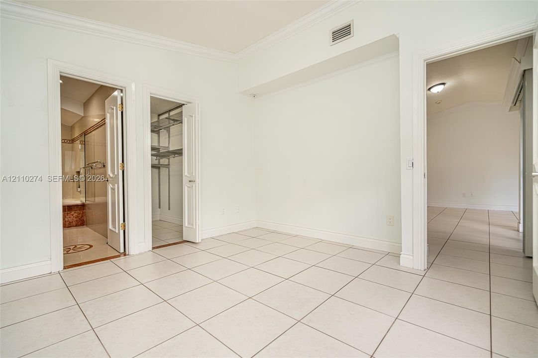 Neutral-toned ceramic tile flooring, solid-core interior doors, walk-in closet with built-in metal shelving, and crown molding