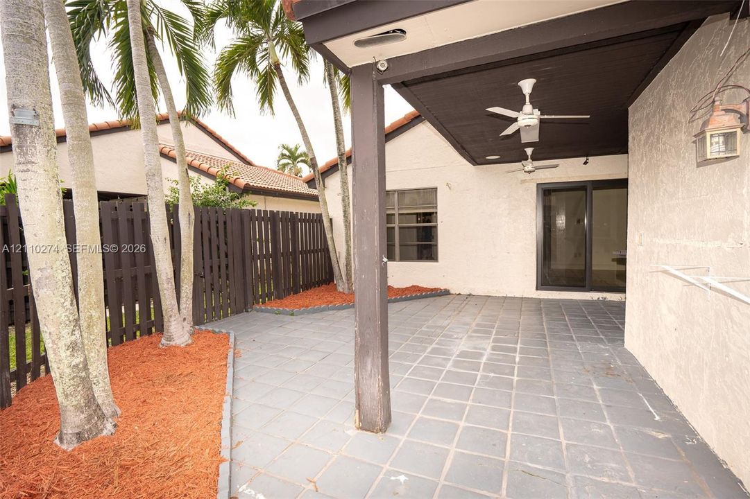 Covered patio with tile flooring, ceiling fans, integrated wall-mounted exterior lighting, and wood-slat fencing