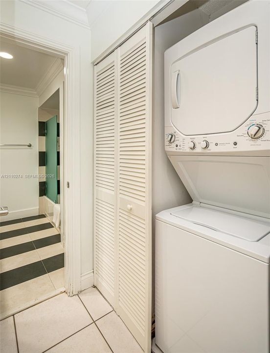 Laundry area featuring a stacked washer and dryer unit, white louvered bifold closet doors, and large-format tile flooring with a black and white striped pattern