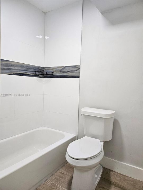 Full bathroom featuring white rectangular wall tile, decorative horizontal inlay, porcelain tub, and wood-finish flooring