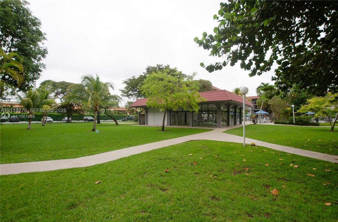 Expansive lawn featuring mature tropical landscaping, concrete paved pathways, and a structure with a red tile roof and expansive glazing