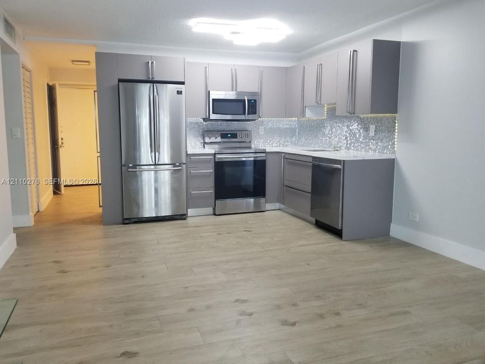 Kitchen featuring flat-panel gray cabinetry, stainless steel appliances, quartz countertops, and a mosaic tile backsplash, complemented by wood-finish flooring
