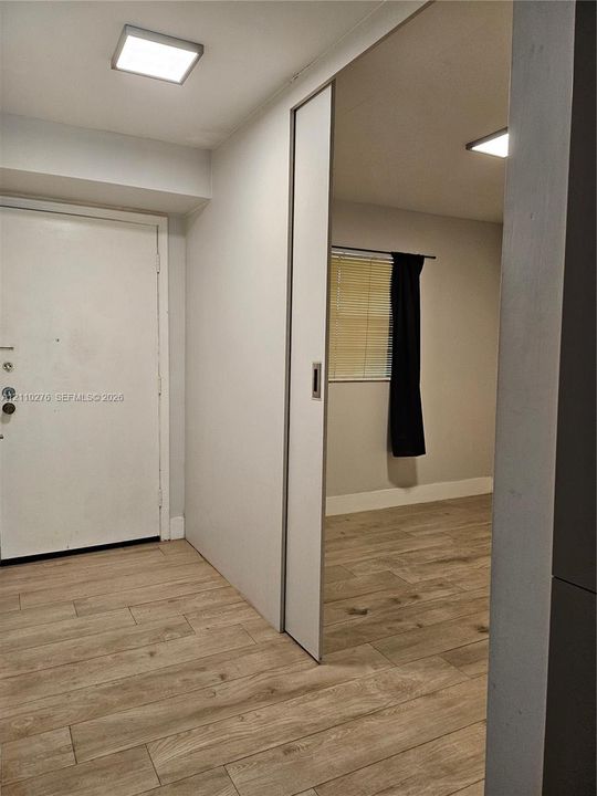 Wood-finish flooring throughout, white interior door, and a sliding panel door with a metallic flush-mount handle