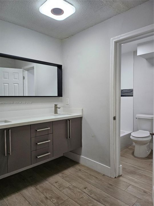 Floating vanity with a smooth solid surface countertop, rectangular undermount sink, integrated cabinetry, wood-finish flooring, and a large-format rectangular wall mirror