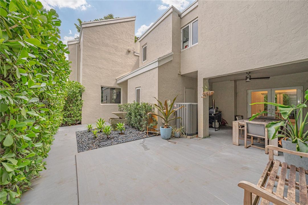 Stucco exterior courtyard featuring a covered patio, stone-accented landscaping, and a privacy hedge