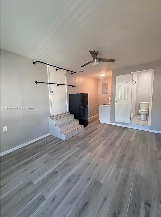 Wood-finish flooring, ceiling fan with integrated lighting, kitchenette area, and multi-panel interior door