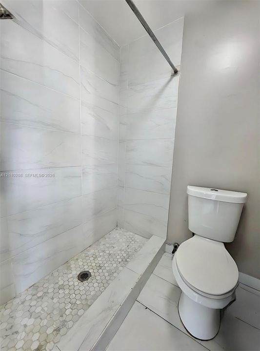 Walk-in shower featuring large-format stone-pattern wall tiles, hexagonal floor tiling, and a metallic shower rod