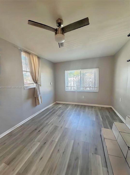 Room featuring wood-finish flooring, dual windows, and a ceiling fan with integrated lighting