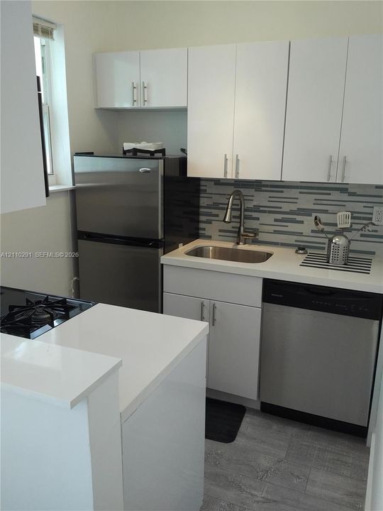 Kitchen featuring white flat-panel cabinetry, stone-composite countertops, stainless steel appliances, multi-tonal linear tile backsplash, and wood-finish flooring