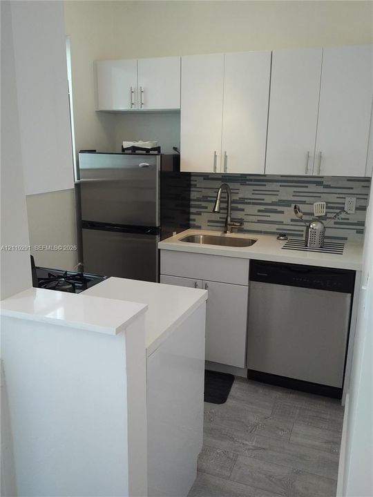 Kitchen featuring white cabinetry, solid surface countertops, stainless steel appliances, multi-toned linear backsplash tile, and wood-finish flooring