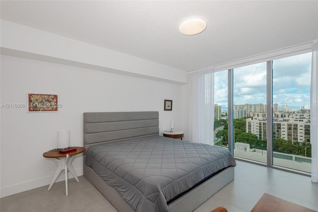 Master Bedroom. Floor-to-ceiling windows, city skyline backdrop, flush-mount lighting, and glass door access to an exterior balcony